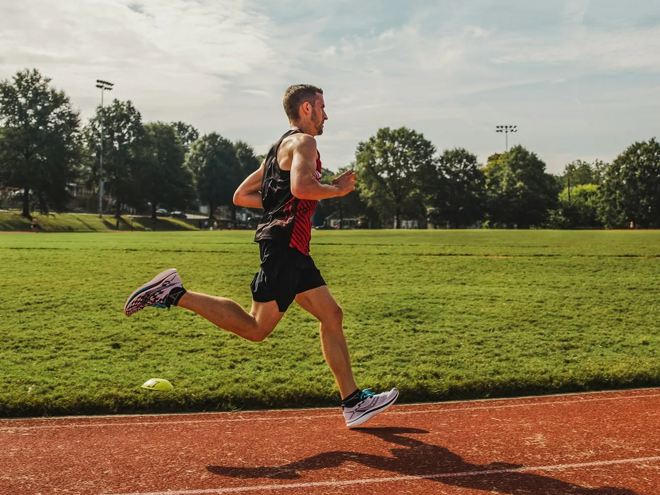 A runner in a racing singlet at full stride on an outdoor running track