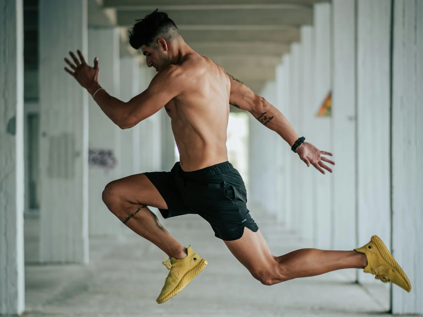 An athlete mid-leap at full stride beneath a concrete colonnade